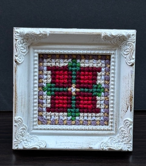 Handmade Christmas cross-stitch in ornate white frame. Folk-art design with red, green, purple threads by North Vancouver artist Kathy Poitras.